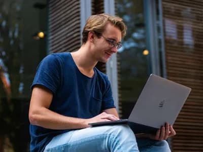 A young professional in a relaxed outdoor setting, possibly attending an online ADHD consultation on his laptop.